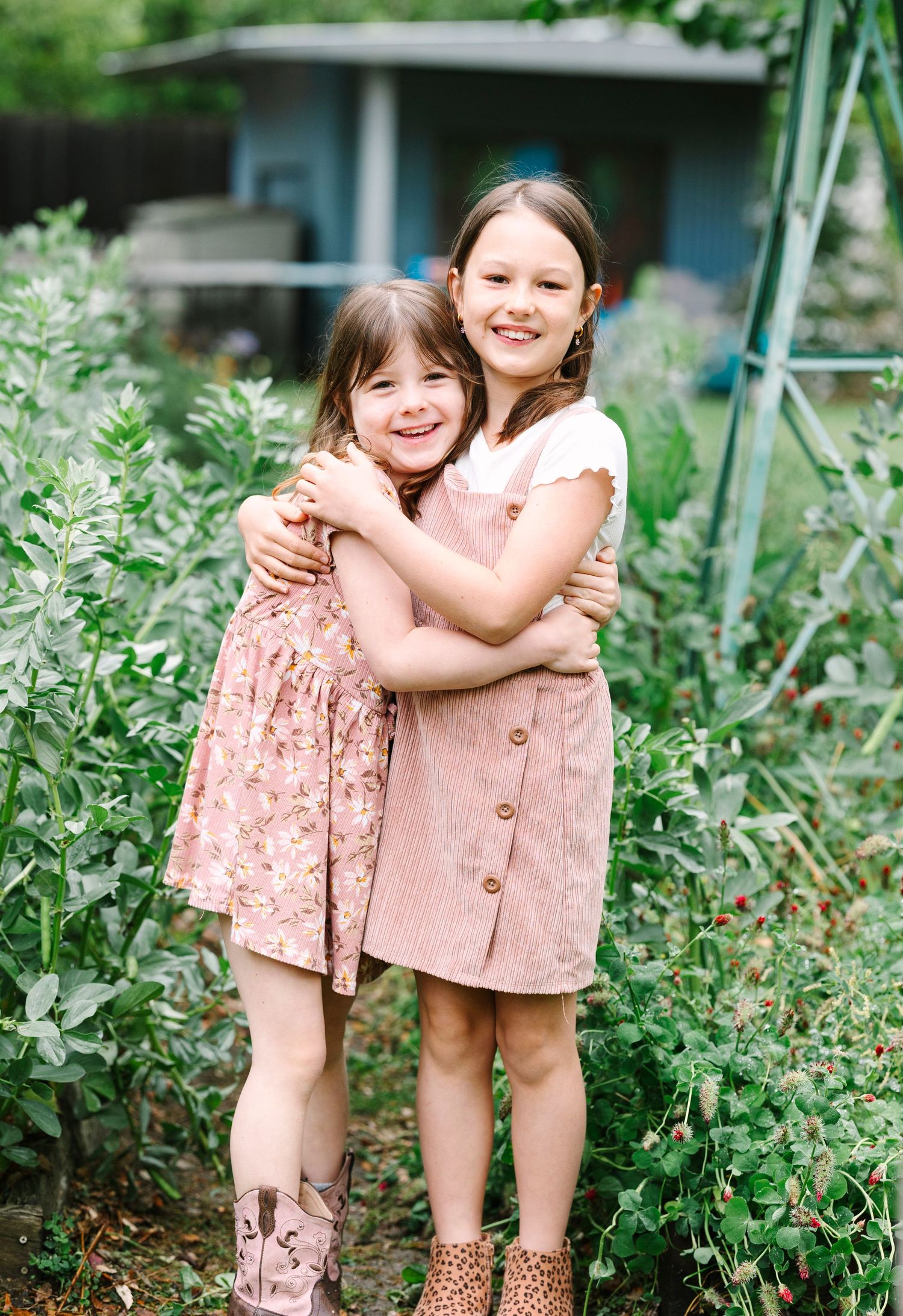 Two children in pink dresses playing in a lush garden setting.