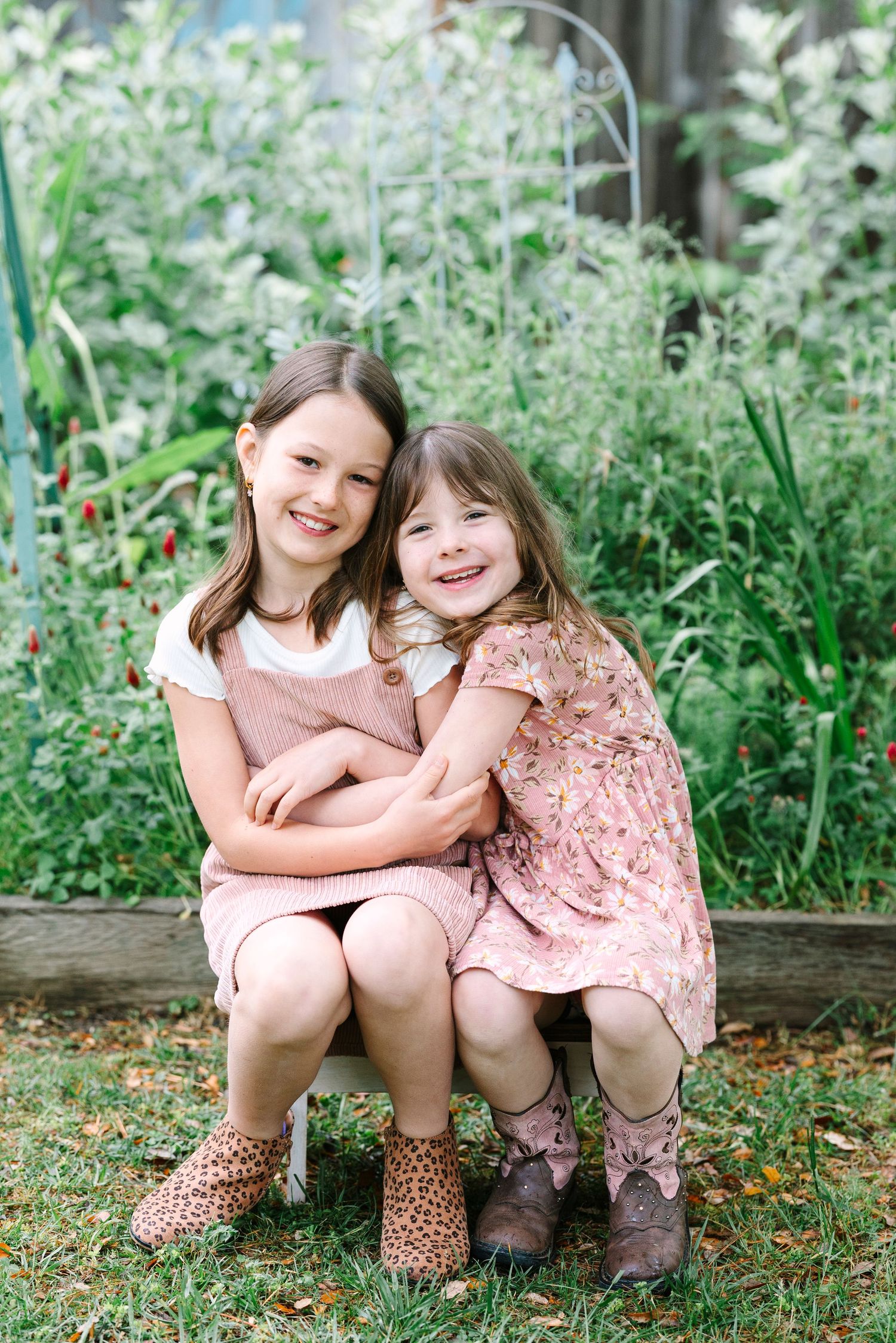 Sisters in matching pink outfits sitting together in garden.