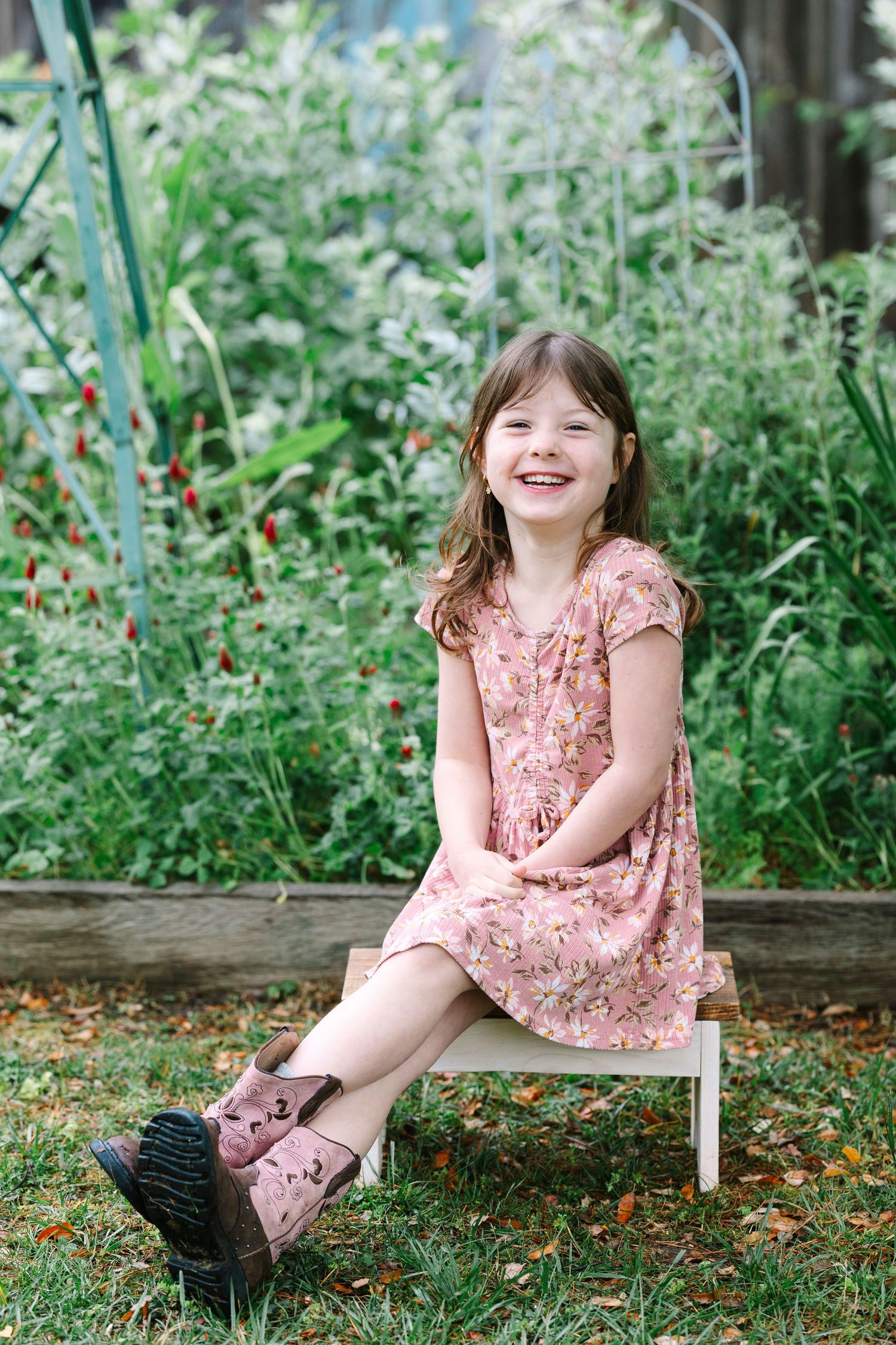 Young girl in pink dress sitting on wooden bench in garden setting.