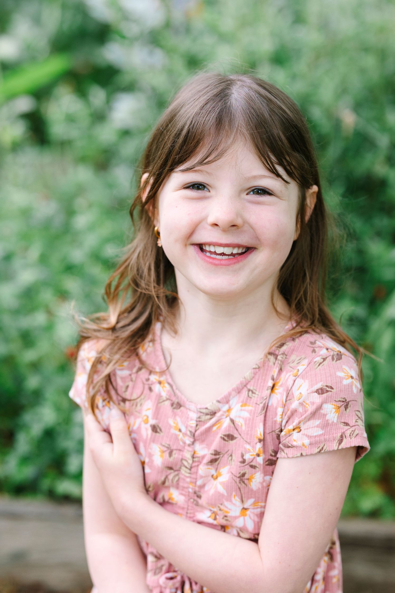Close-up portrait of child in floral pink dress against green garden background.