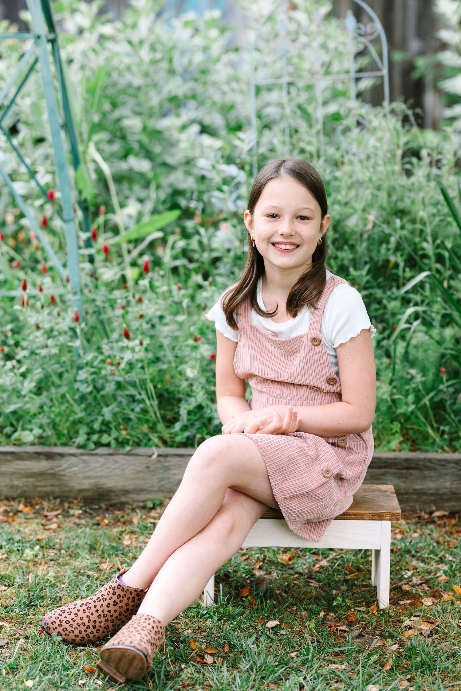 Child in pink dress sitting casually on white bench outdoors.
