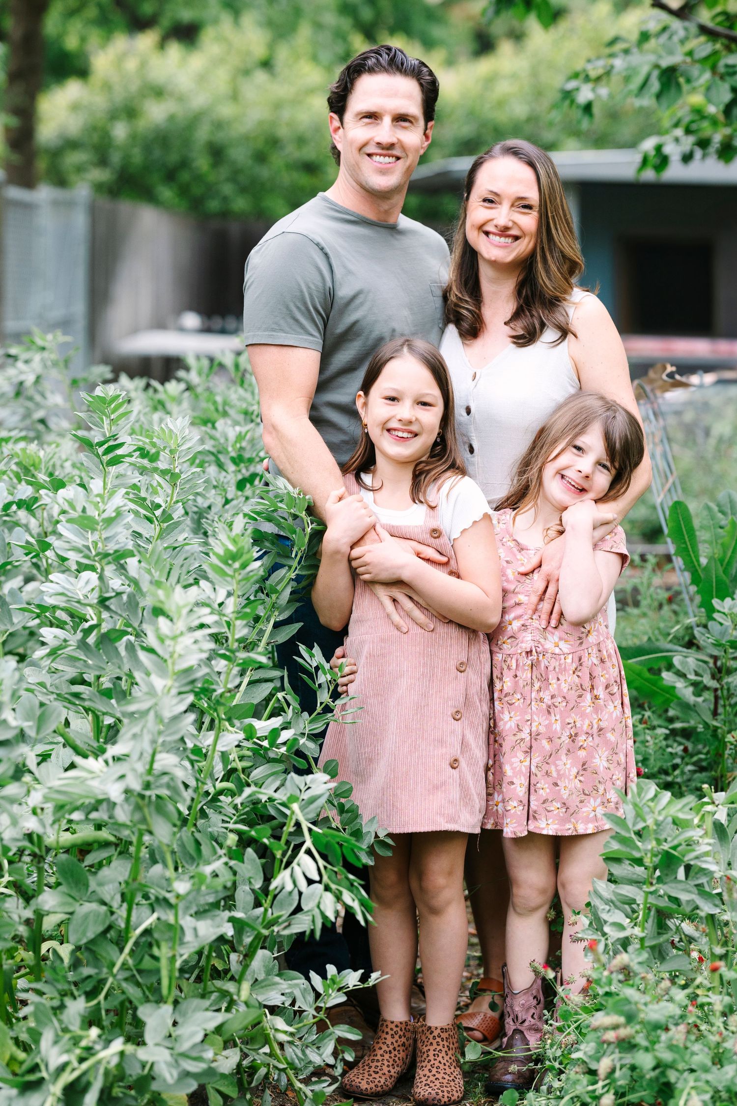 A family of four poses together outdoors surrounded by green foliage.