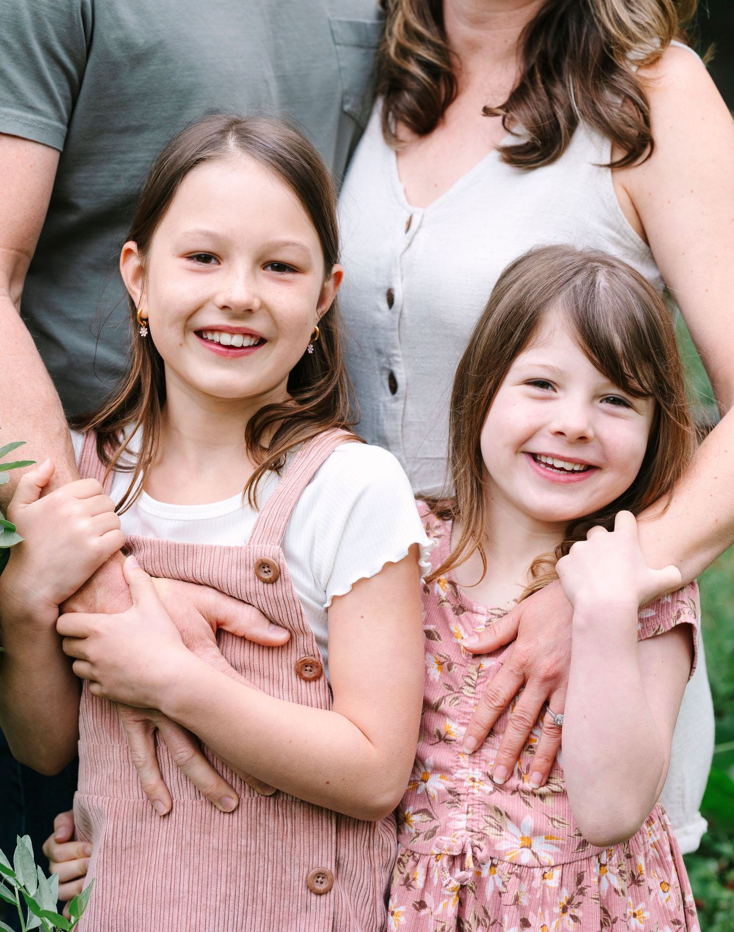 Two children in pink dresses smile brightly while being held by their parents.