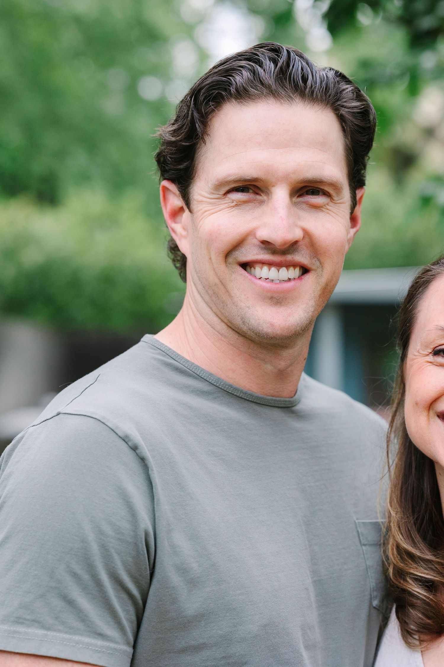 A close-up portrait of someone in a grey t-shirt smiling warmly at the camera.