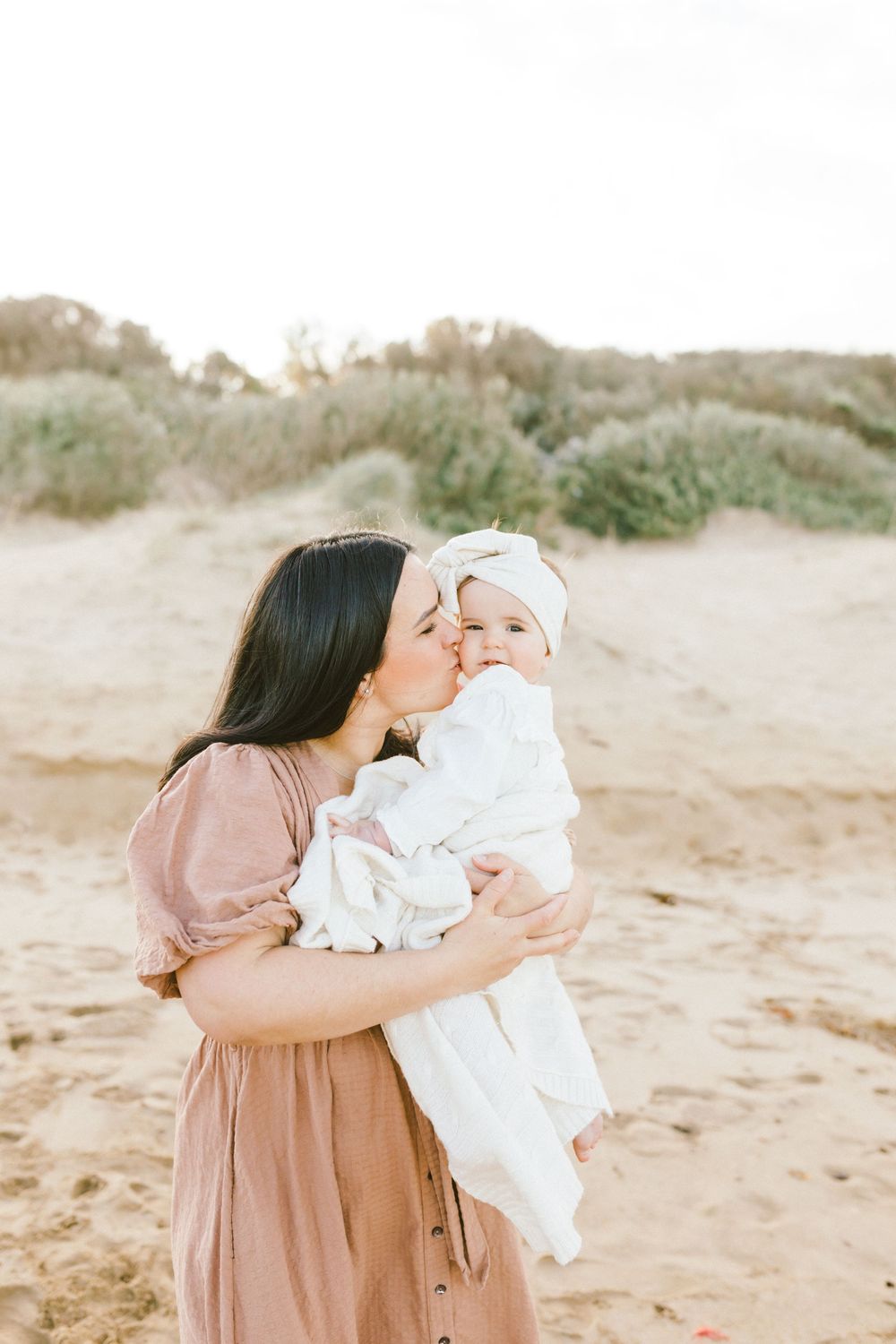 A tender moment captured in a series of soft, beige-toned photos on a sandy beach setting.