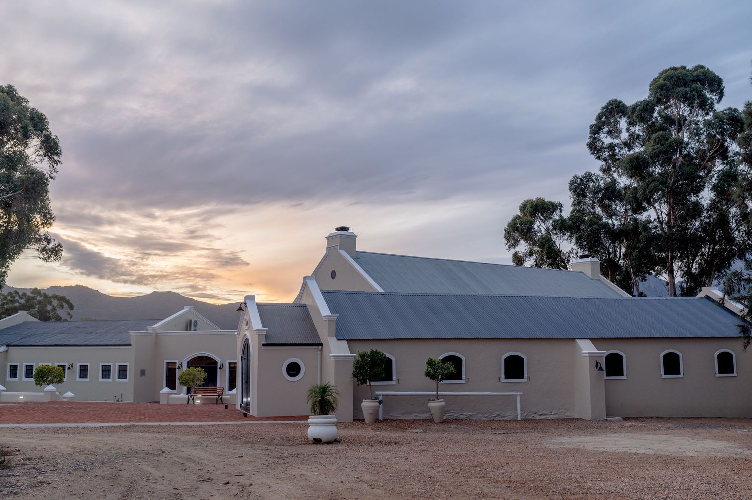 A panoramic view of white farm buildings with arched windows against a cloudy sky at sunset.