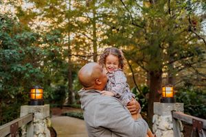 Family enjoying a warm sunset moment together in a park setting with golden sunlight filtering through trees.