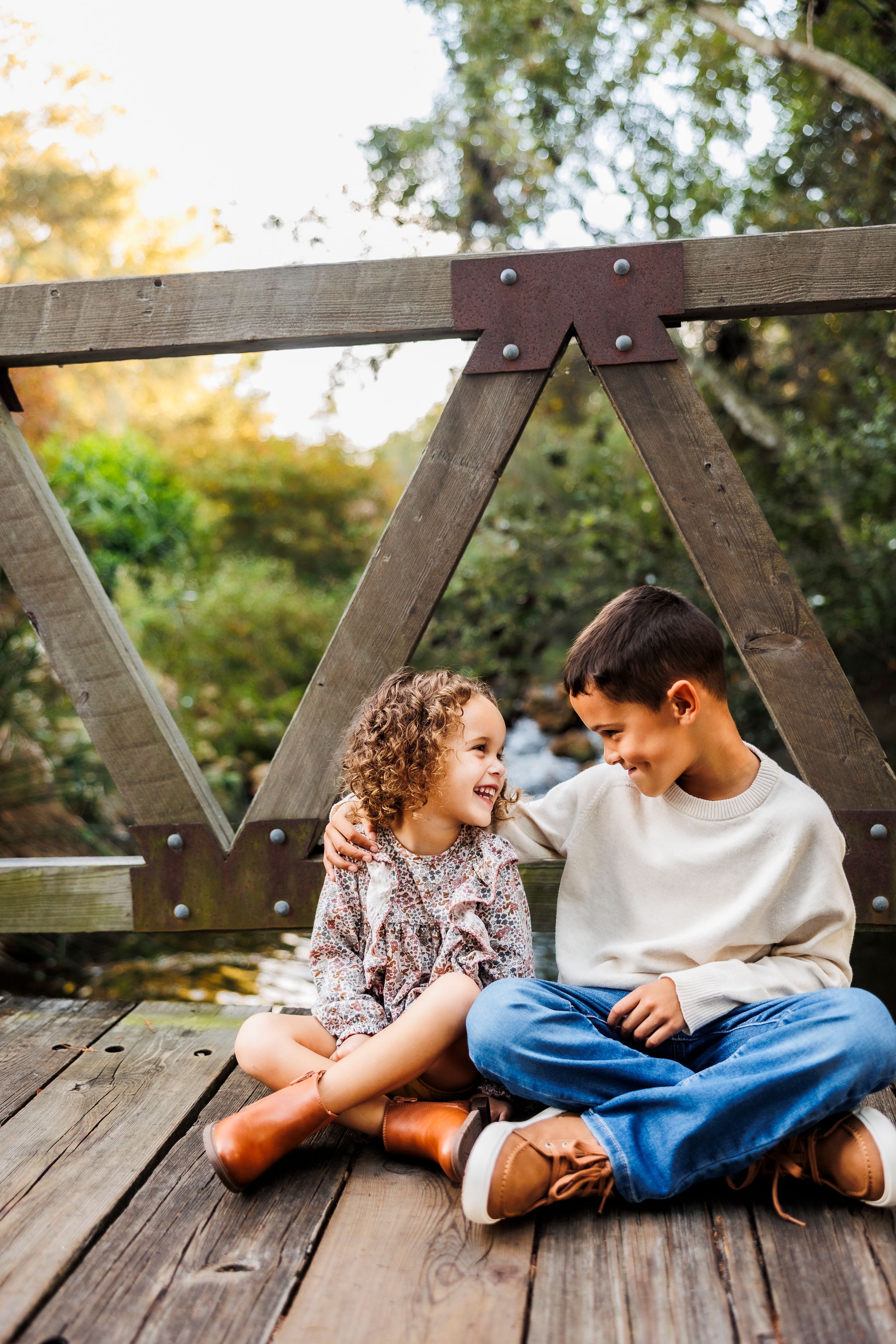 Two children share a sweet moment lying on a wooden deck during golden hour.