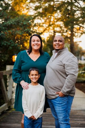 Family portrait session on a wooden boardwalk at sunset with warm golden light filtering through trees.