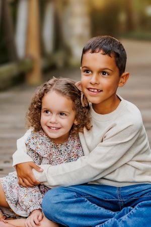 Two siblings share a tender moment in matching outfits while sitting together during an outdoor photo session.
