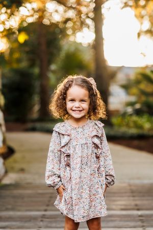 Young child in floral dress smiling during golden hour outdoor photoshoot.
