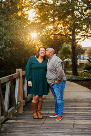 A couple shares tender moments at sunset on a wooden bridge surrounded by autumn trees and golden light.