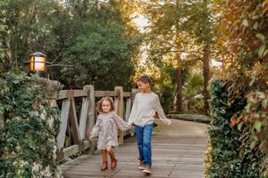 Two children walk hand in hand down a tree-lined garden path at sunset during autumn.