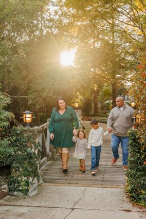 Family walking together on a wooden bridge path during golden hour with sunlight streaming through autumn trees.