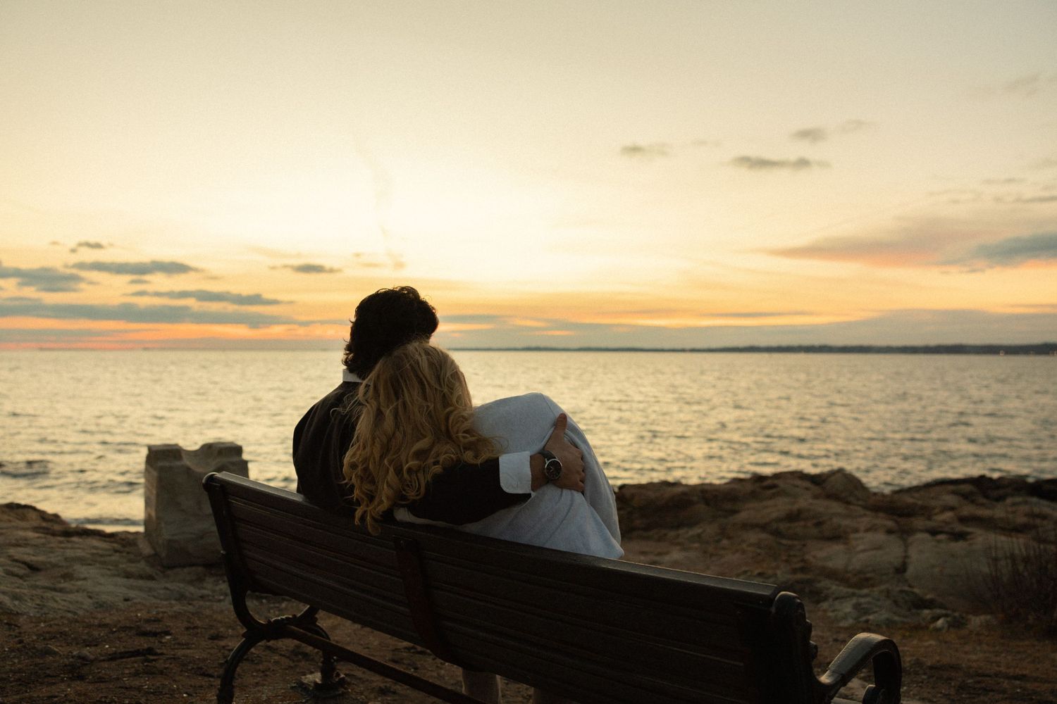 Two people sharing a quiet moment watching the sunset together on a bench by the ocean.