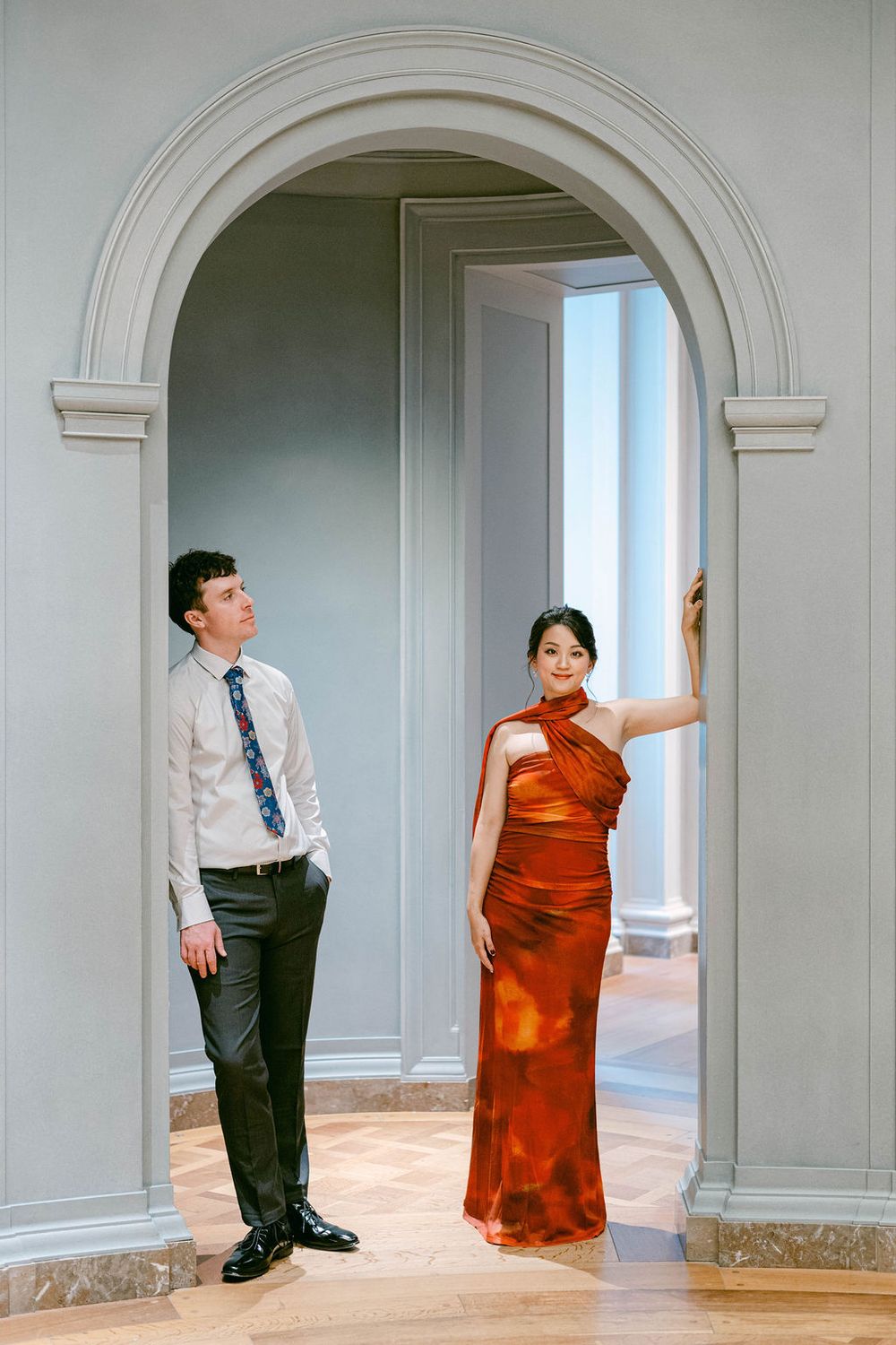 A couple poses playfully in a series of shots under elegant arched doorways in a classical interior.