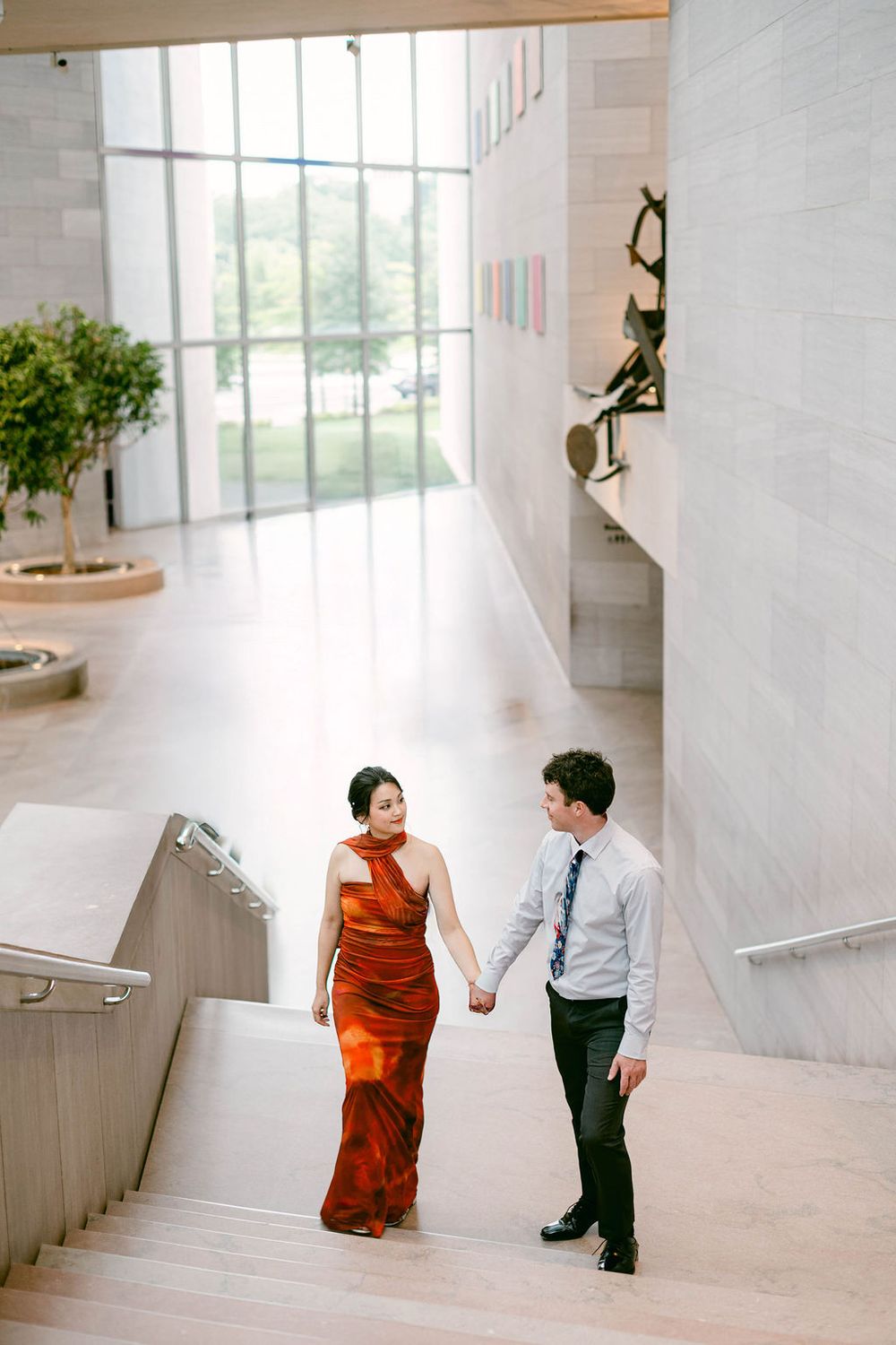 A couple walks together through a bright modern interior with white walls and large windows.