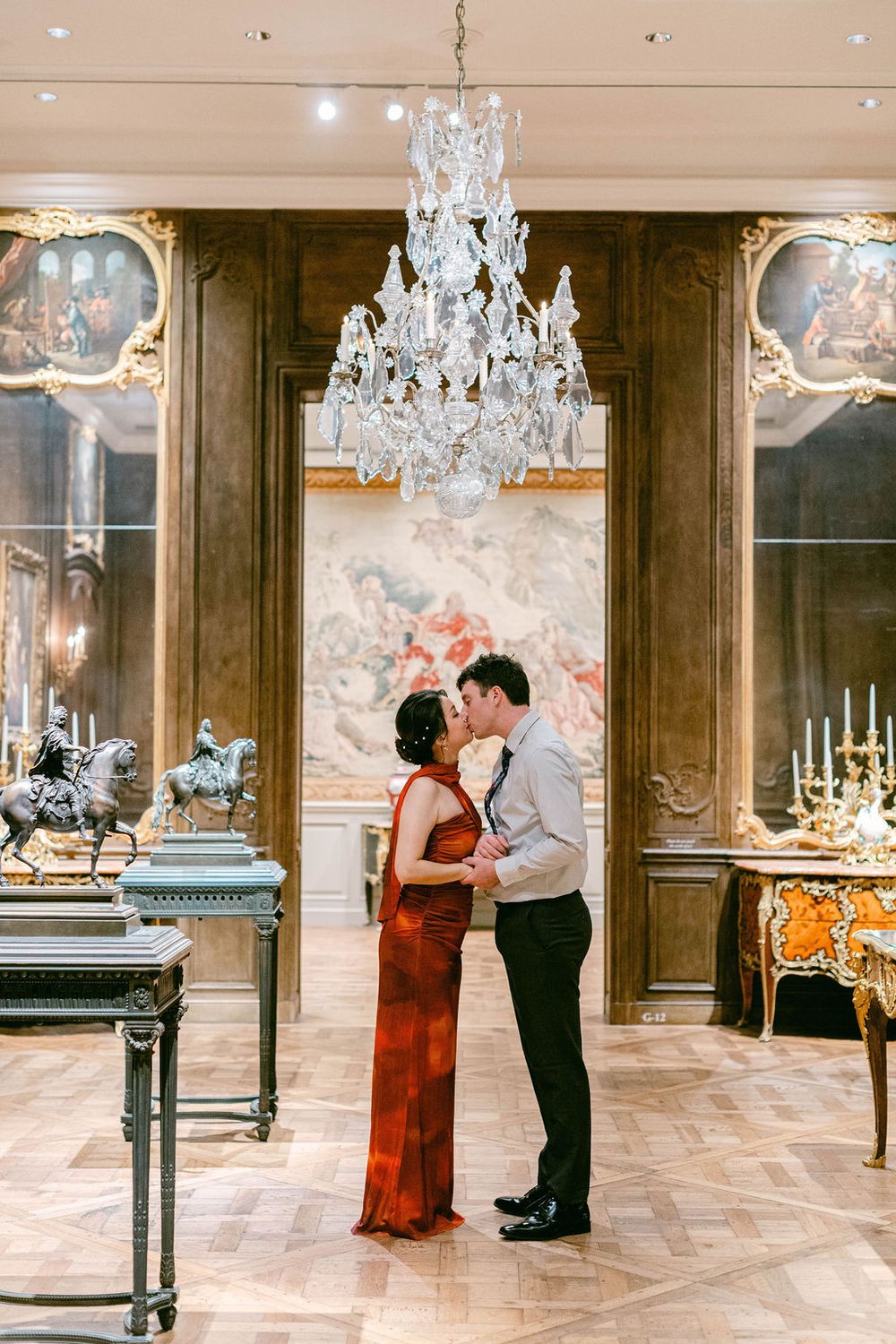 A couple shares an intimate moment in an elegant ballroom with crystal chandeliers and ornate decor.