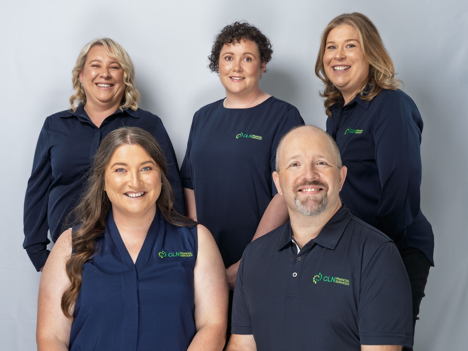 Group of five professionals in matching navy polo shirts pose together for a team photo.