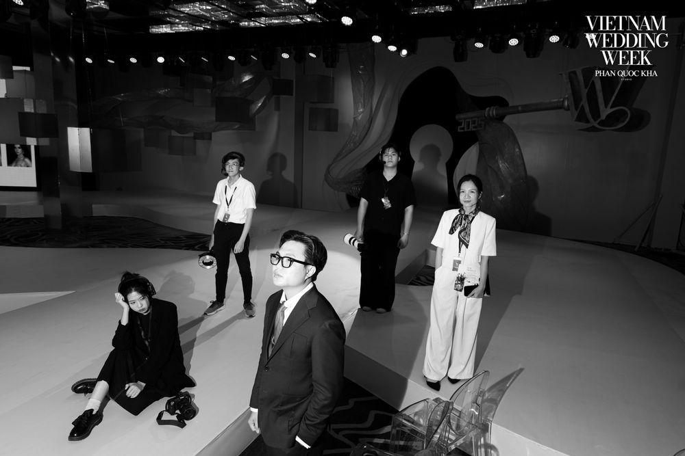 Black and white group photo at Vietnam Wedding Week fashion event with five elegantly dressed attendees posing dramatically.