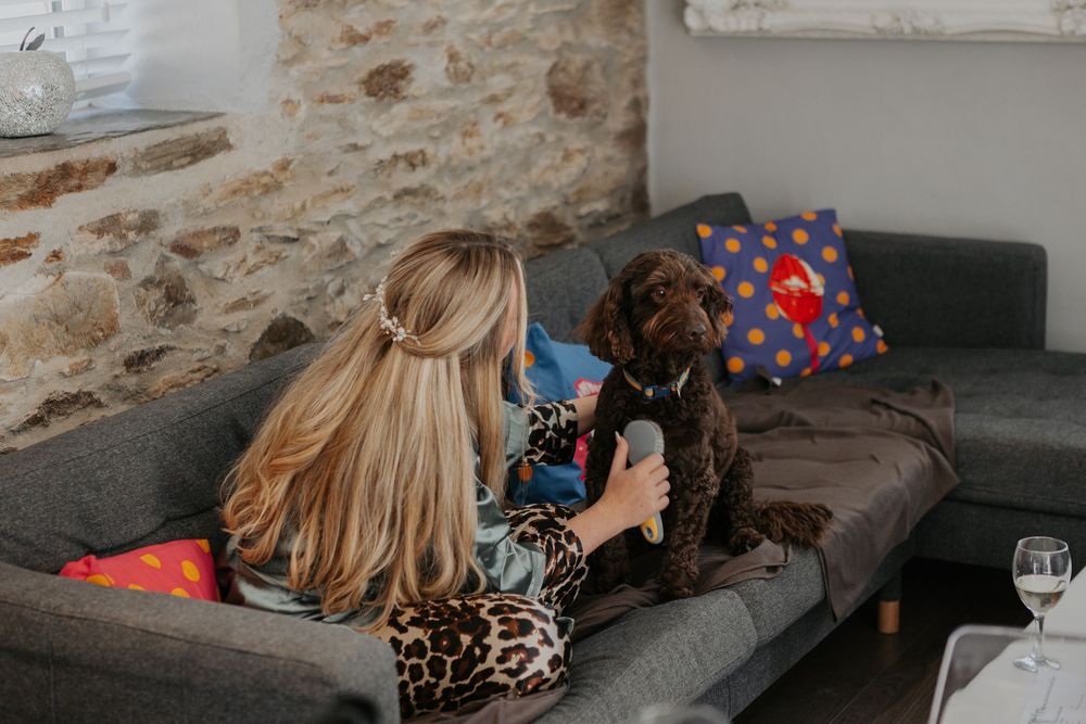 Bride in leopard print robe relaxing on a grey sofa with a brown curly dog during wedding morning preparations.