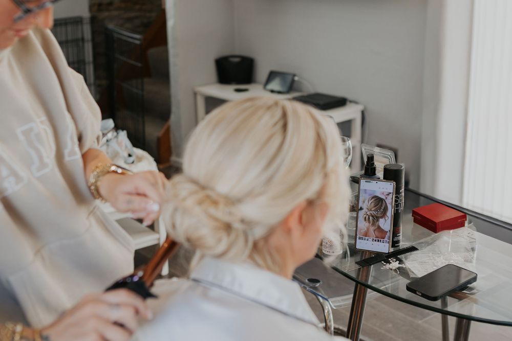 Hair stylist creating an updo hairstyle for a blonde bride using a photo reference.