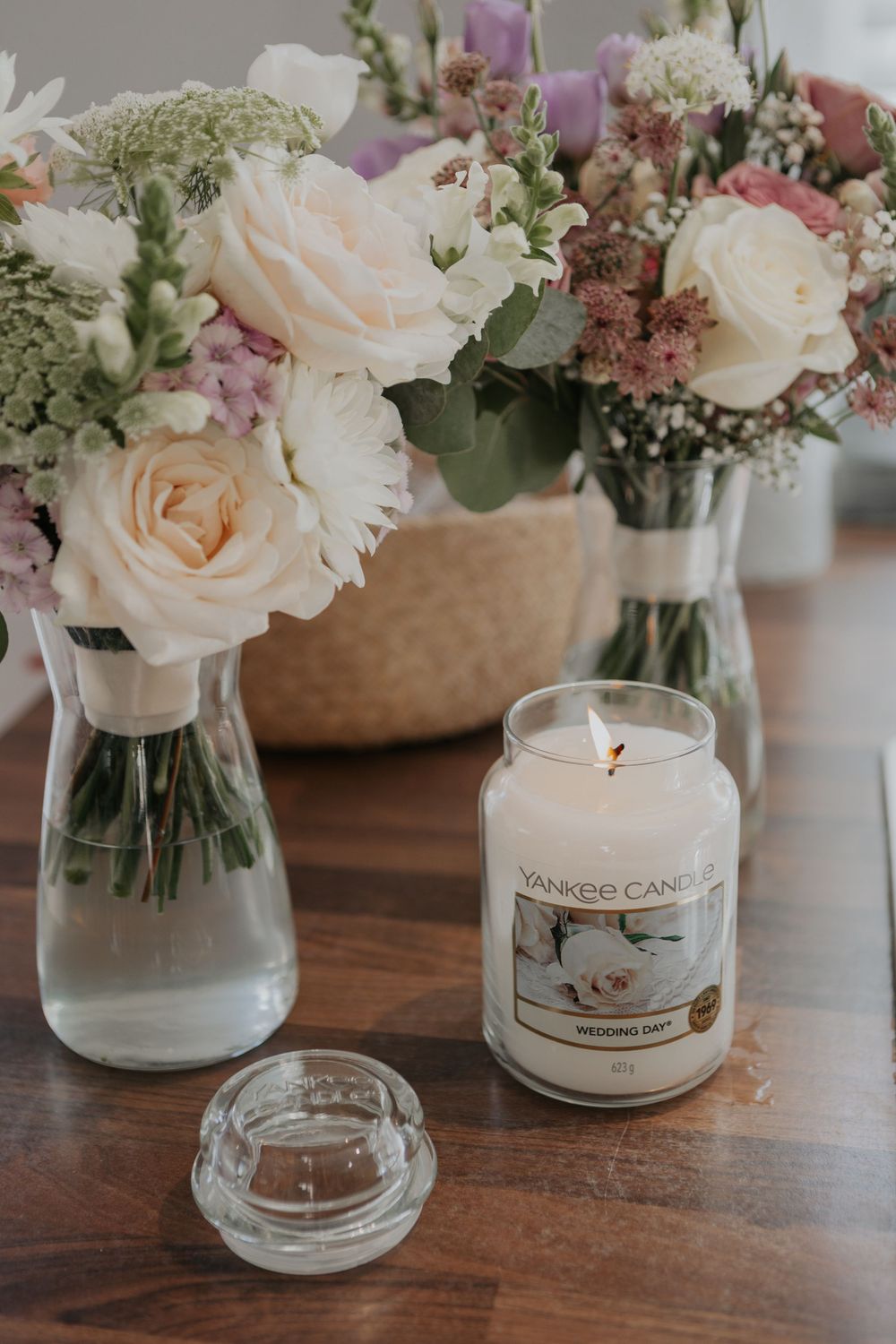 Yankee Wedding Day candle surrounded by pink and white rose bouquets on wooden table.