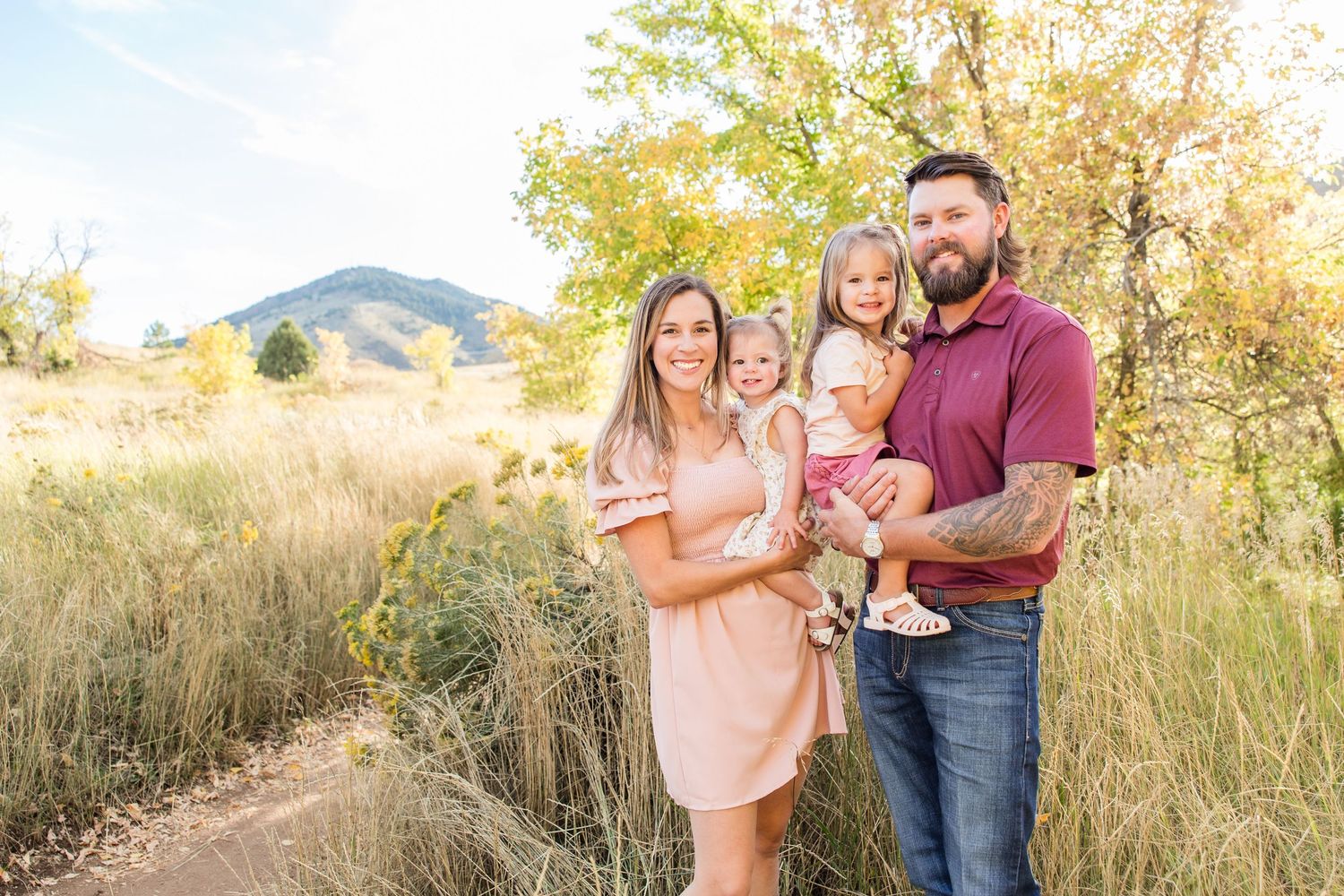A family poses together in a golden field at sunset with mountains in the background.