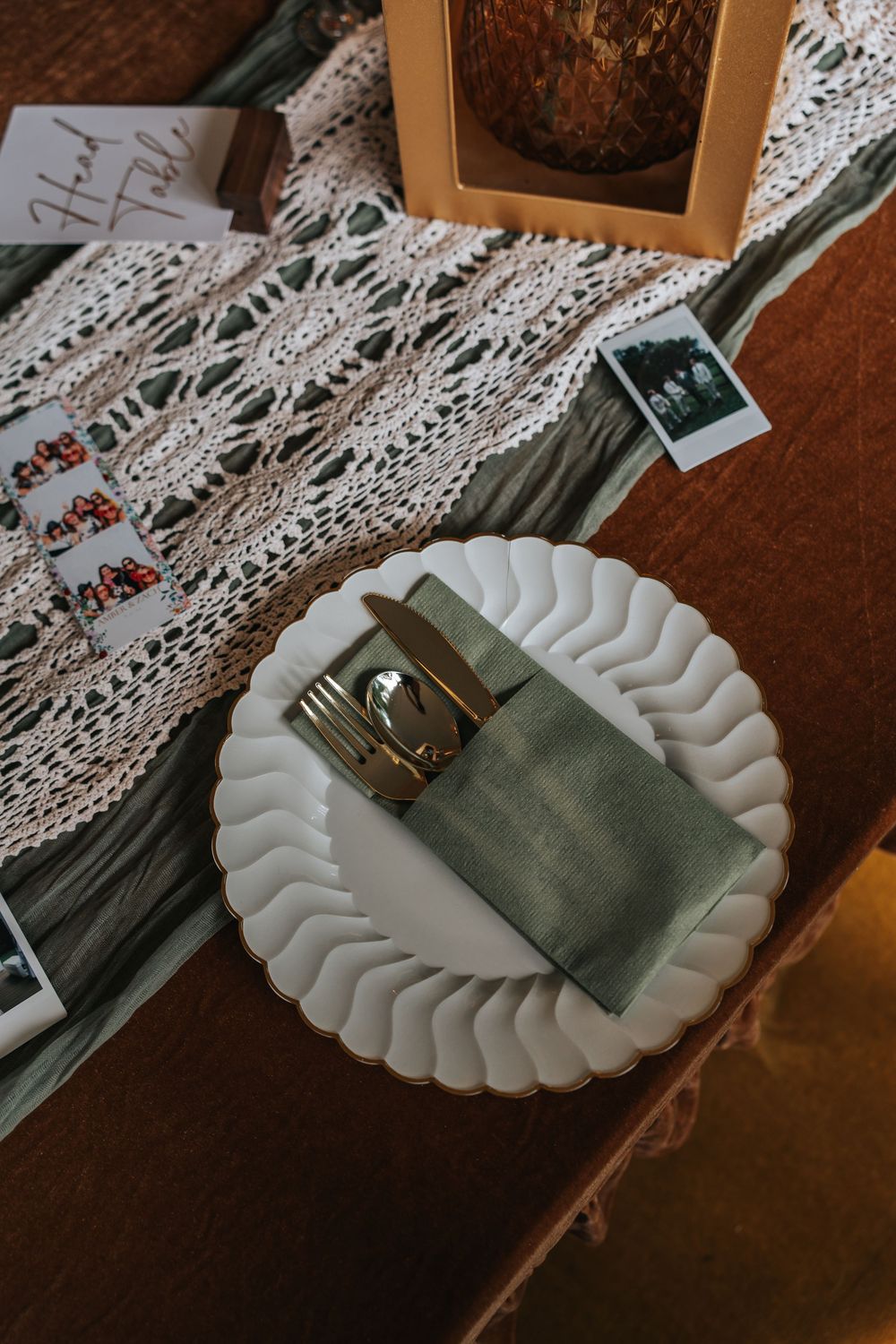 White scalloped plate with sage green napkin and silverware on delicate lace tablecloth.