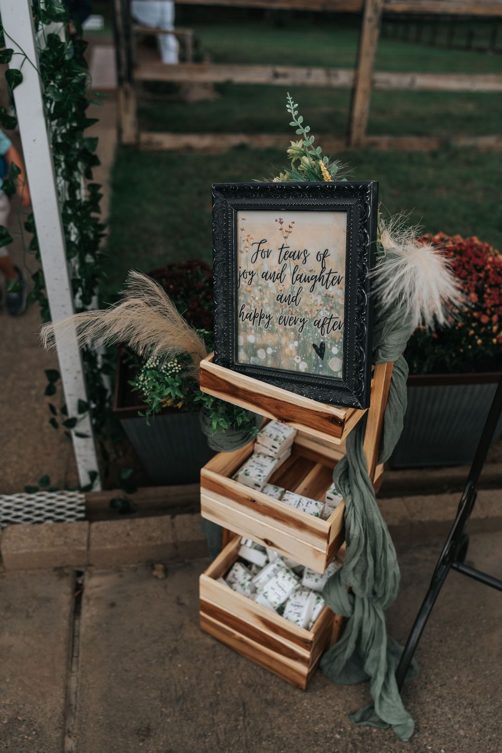 Rustic wooden display stand with decorative signs and fabric draping at an outdoor wedding venue.