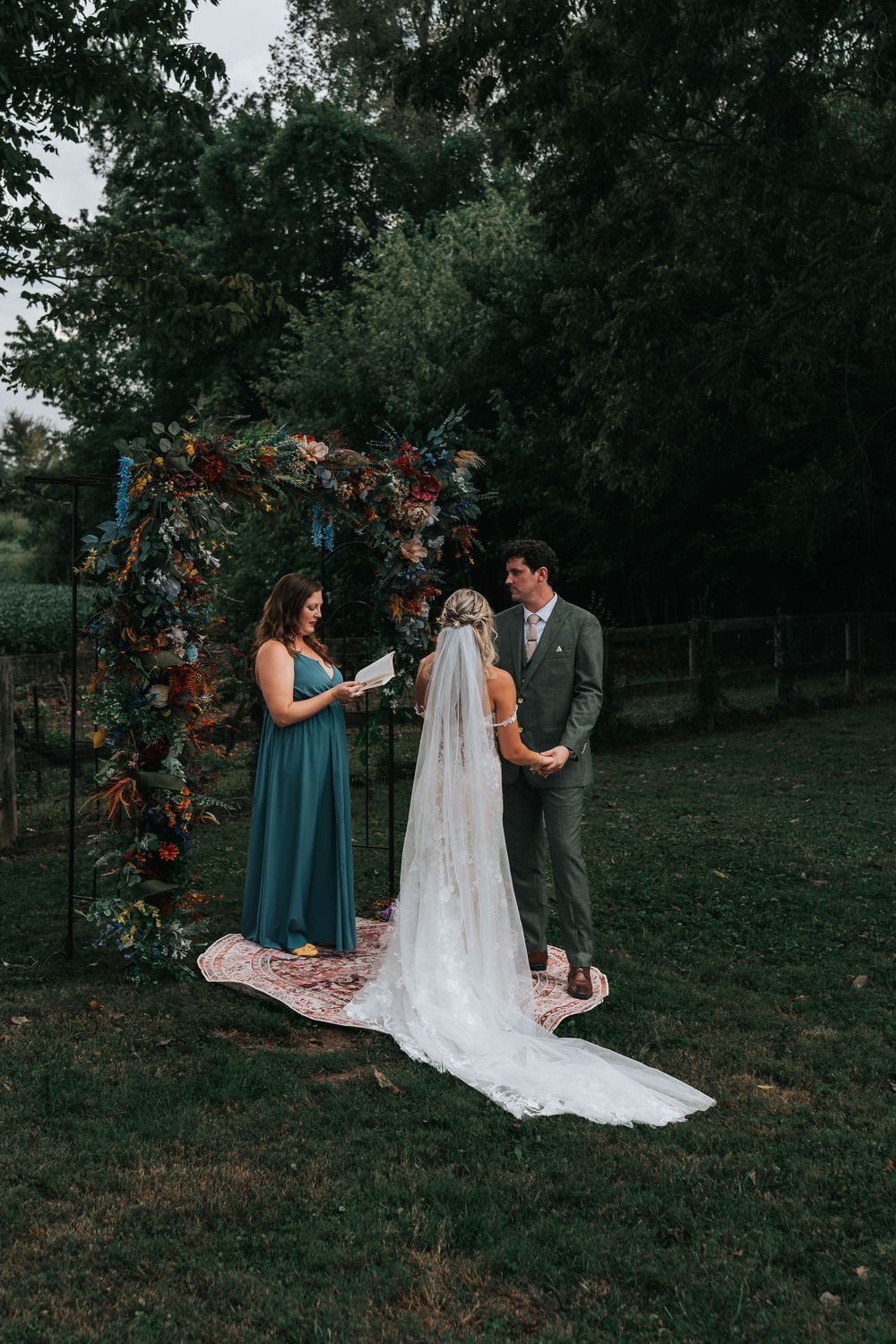 An outdoor wedding ceremony setup with a floral arch and flowing white dress against a backdrop of lush greenery.