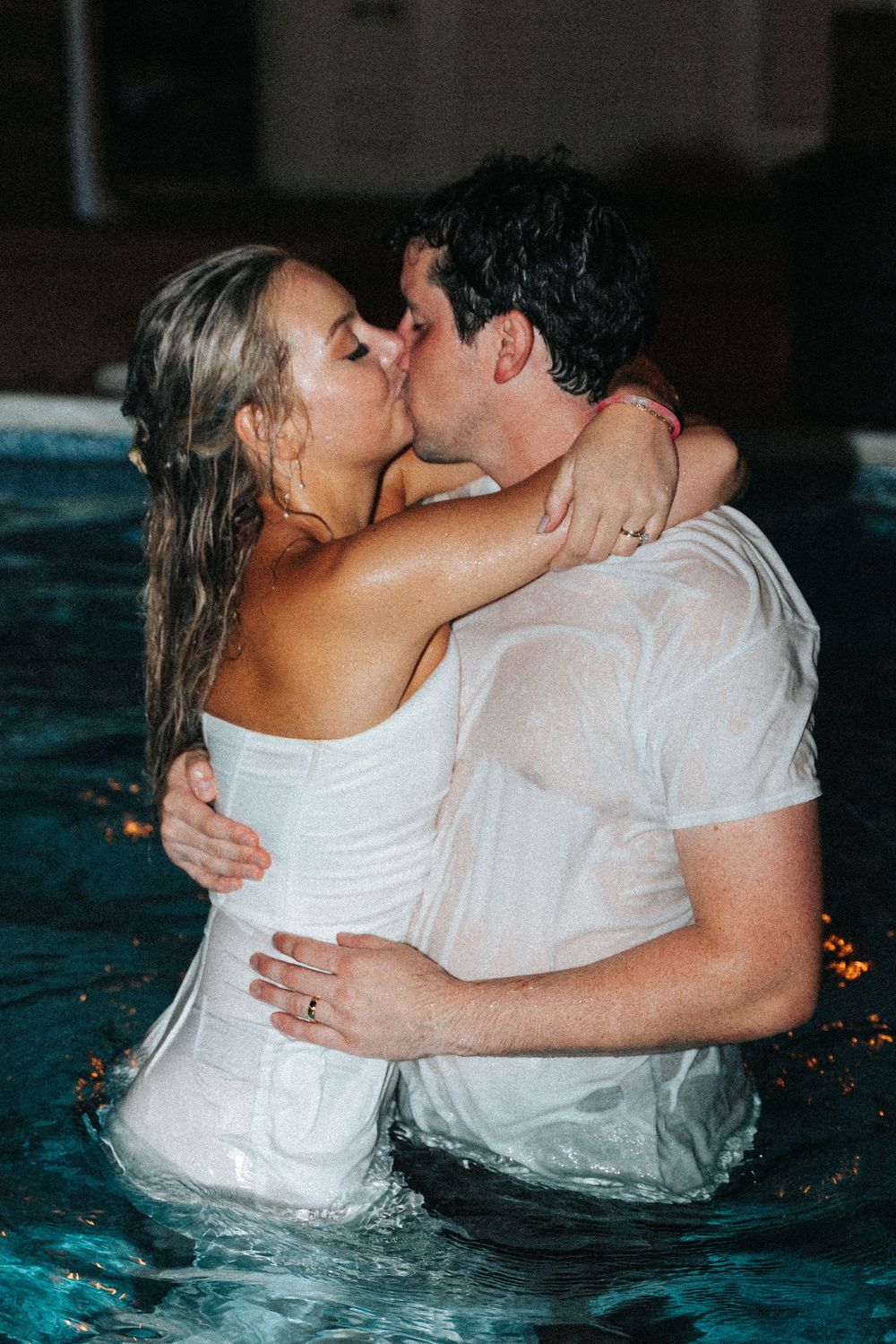 Newlywed couple sharing intimate moments in a swimming pool while wearing wedding attire.