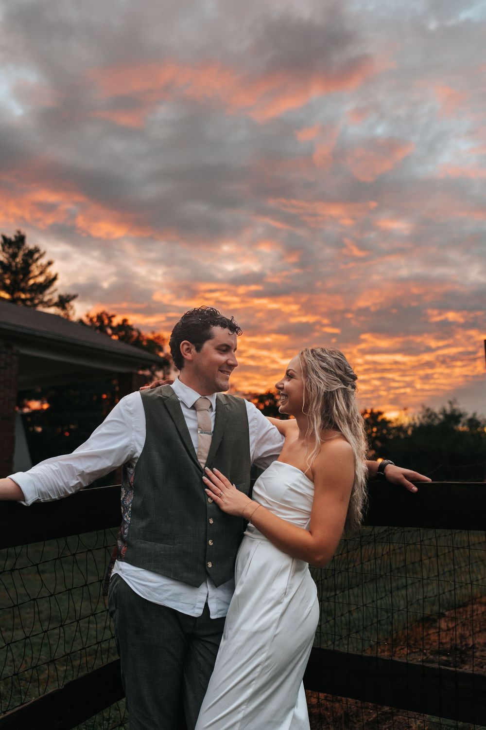 A couple shares a romantic dance at sunset with dramatic orange and gray clouds in the background.