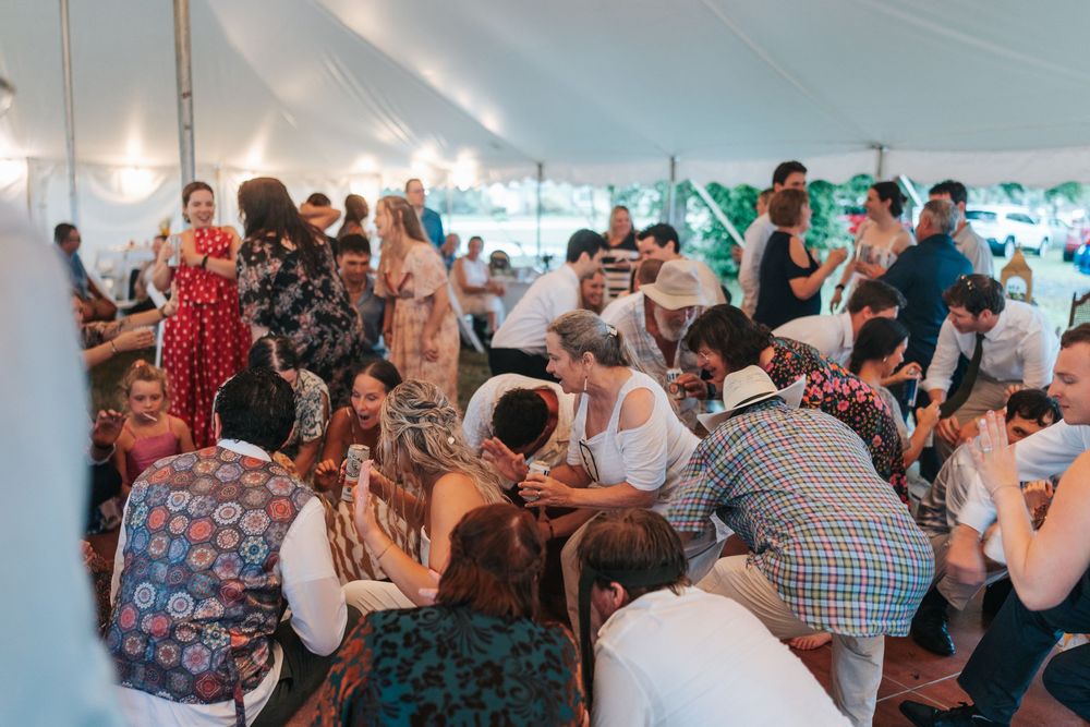 Large wedding reception under a white tent with guests seated at round tables.