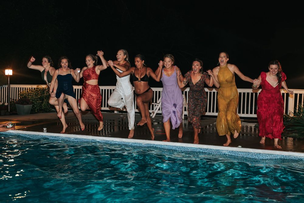 Wedding party jumping into a swimming pool at night during celebration.