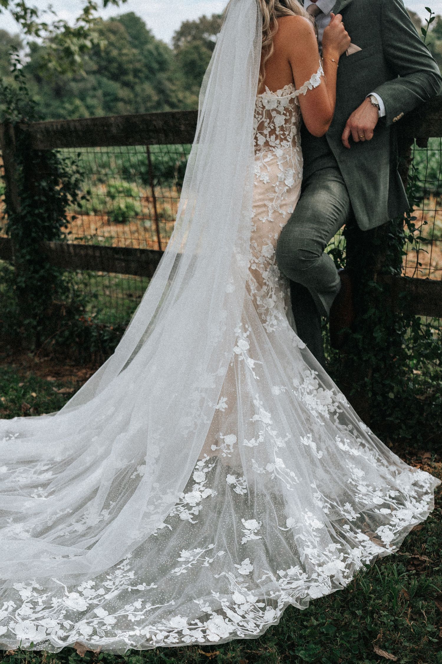 A stunning lace wedding dress with intricate floral details and a long flowing train captured in an outdoor garden setting.