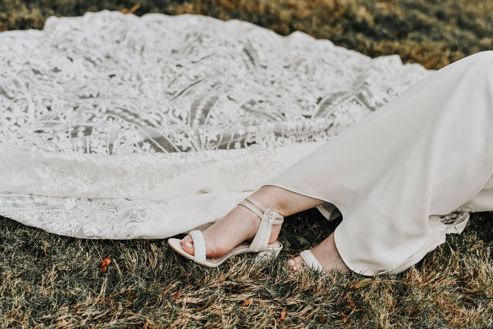 a close up photo of a brides wedding heels as their draped in the lace from her wedding gown