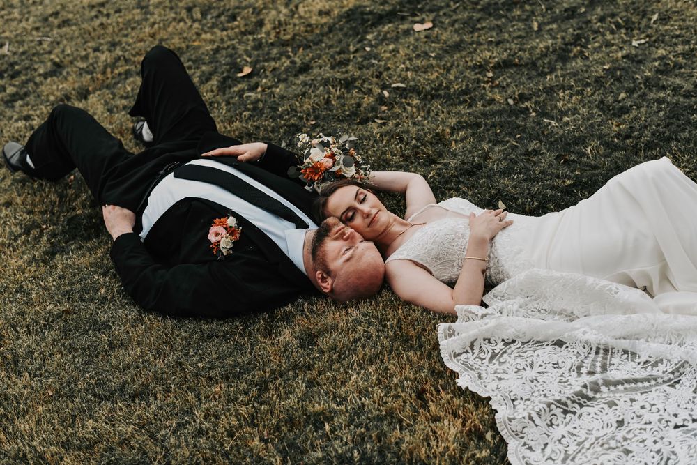 an editorial shot of a bride and her groom laying on the grass looking at the sky