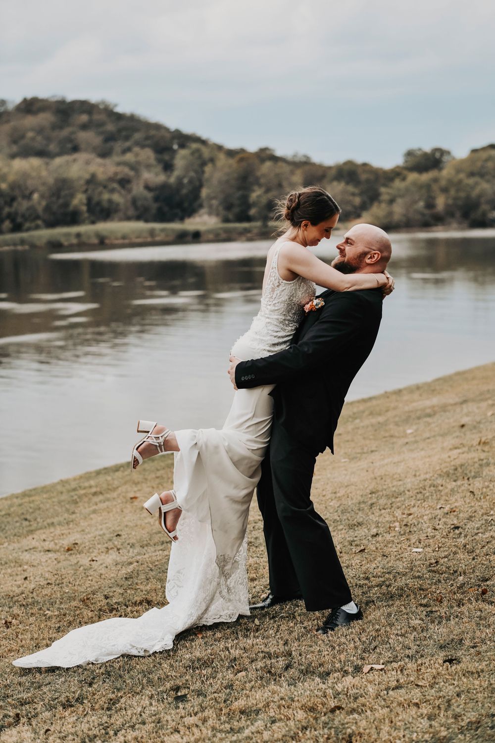 a groom playfully lifts his bride as her wedding gown flows romantically