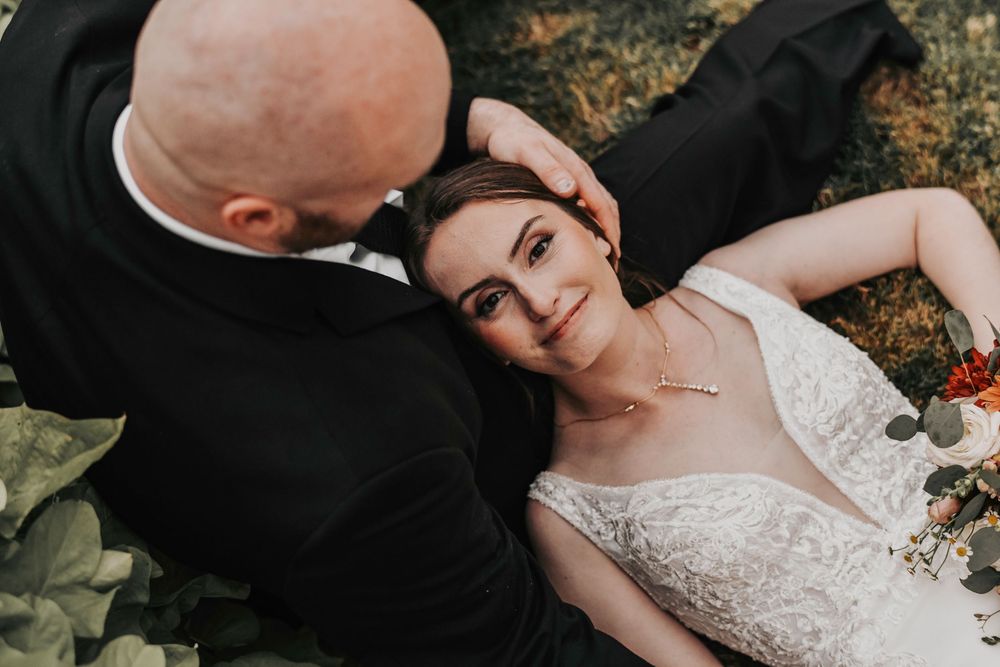 the bride looks directly into the camera as her husband caresses her hair