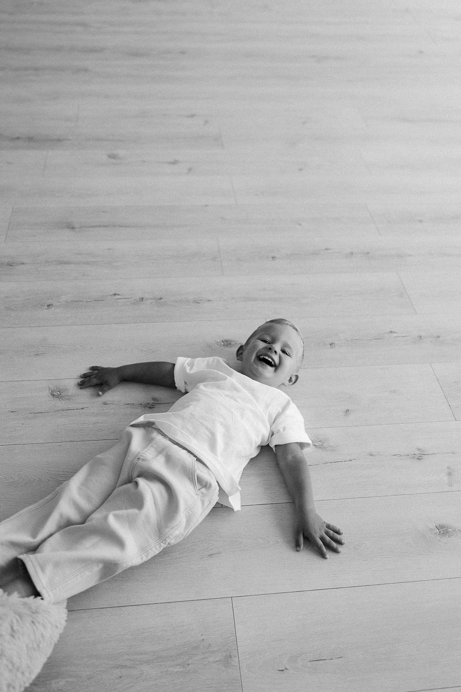 A baby wearing white clothing lies on a wooden floor laughing joyfully in a series of connected photos.
