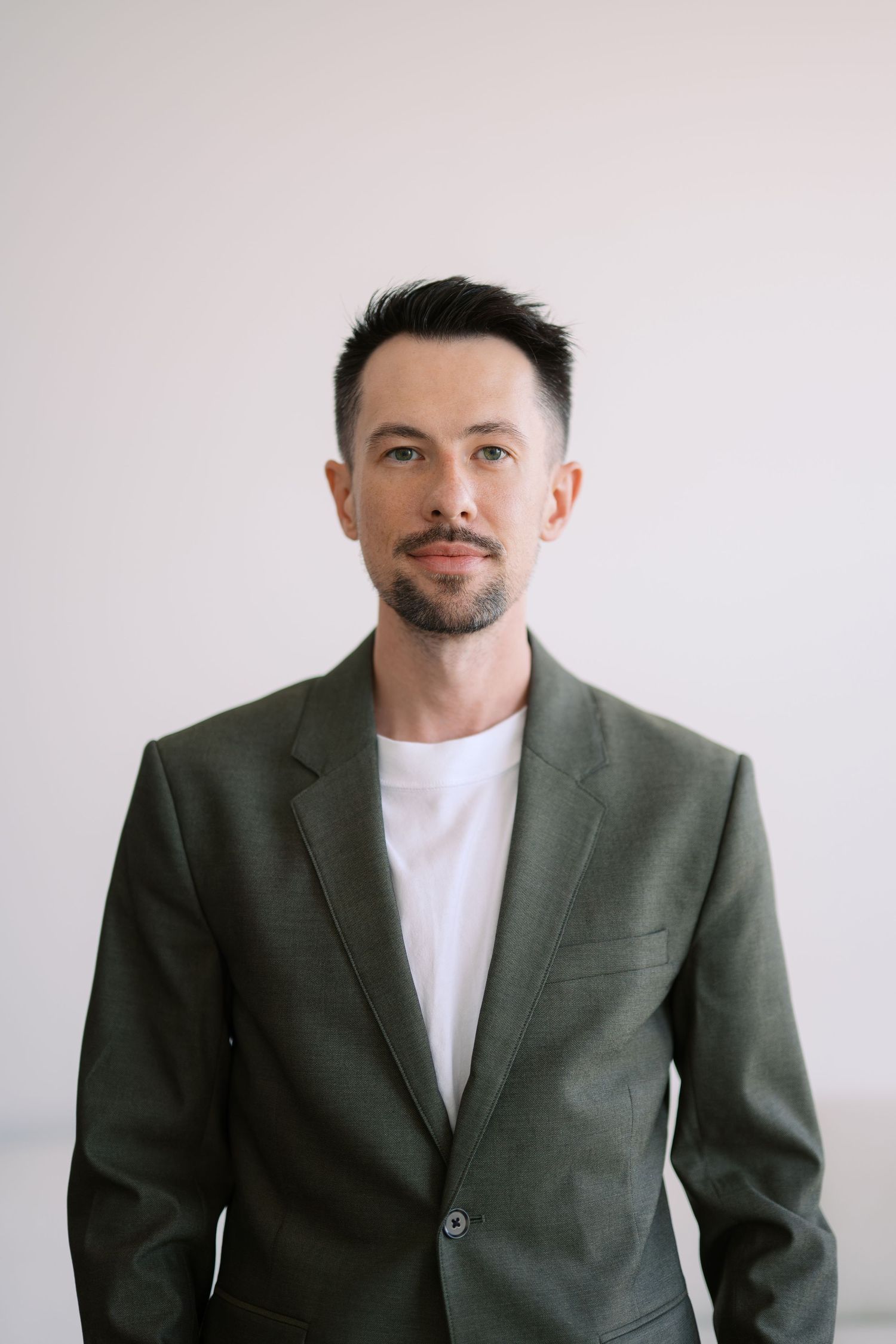Professional portrait of person in gray suit jacket and white t-shirt against light background.