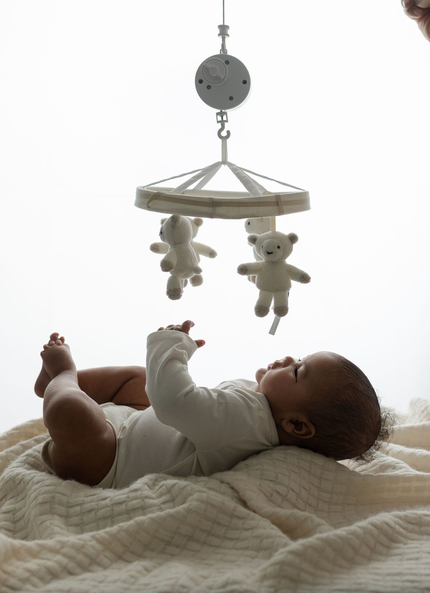Unedited backlit image by Charlottesville baby and newborn photographer shows a boy reaching toward a mobile during his milestone session.