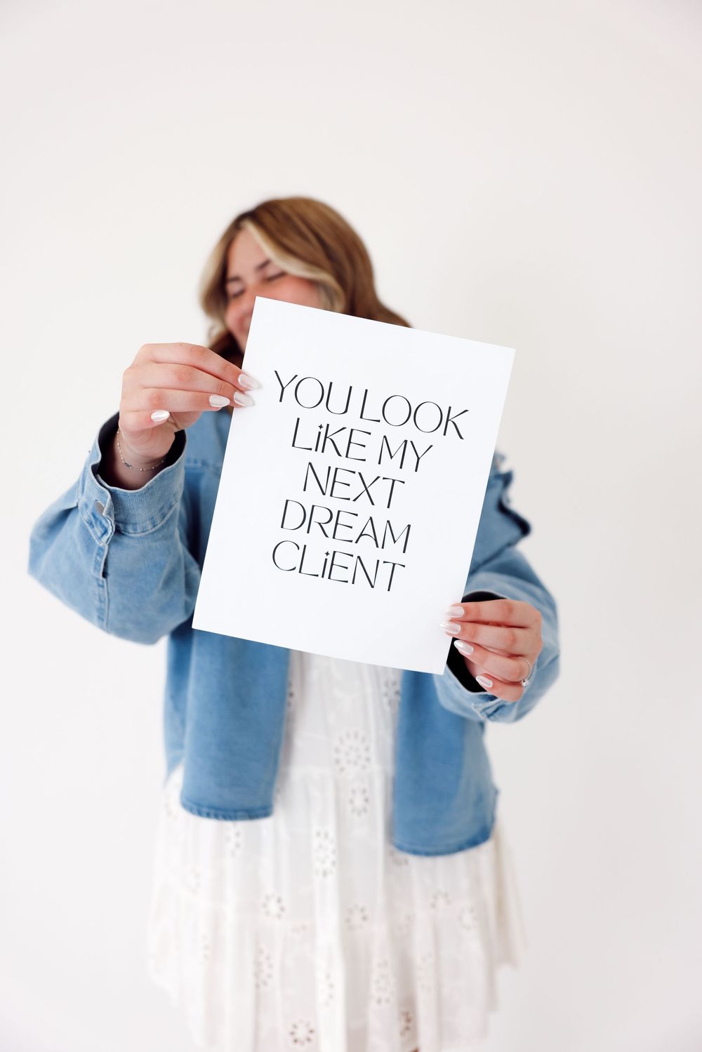 Person in denim jacket and white dress holds up series of text signs in sequential photos.