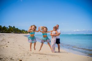 Family of four joyfully jumping on a tropical beach with turquoise water and clear blue skies.
