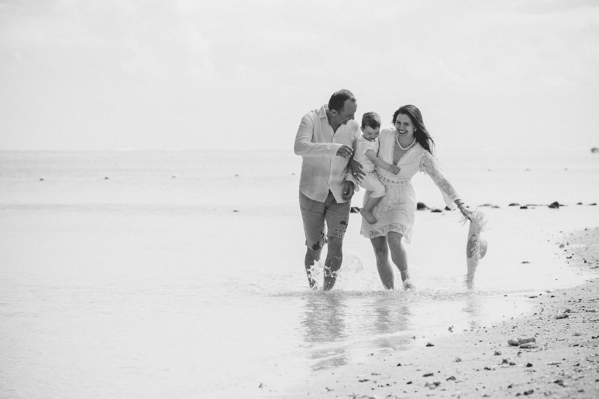 Black and white photo of a happy family playing in ocean waves on a sandy beach.