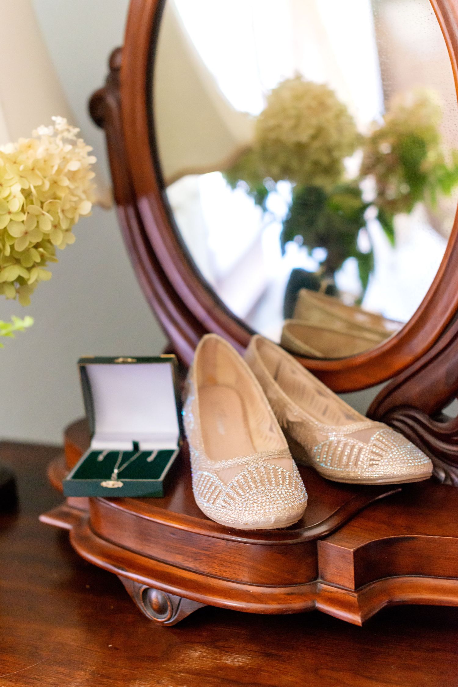 Elegant beaded bridal flats displayed on antique wooden dresser beside green jewelry box with necklace and oval mirror.