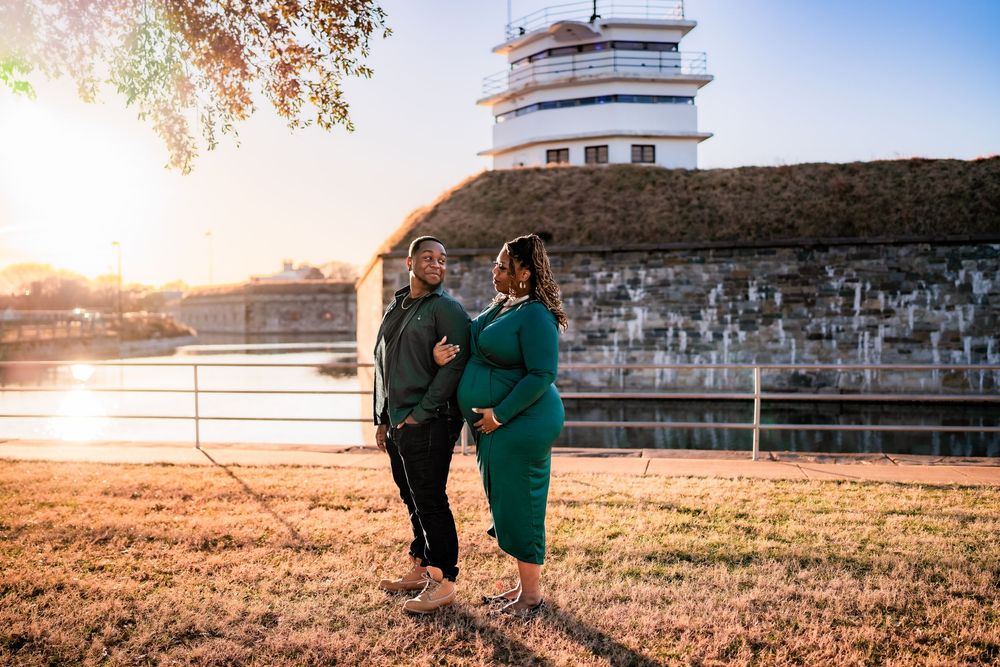 Couple poses together at sunset near historic stone building by waterway.