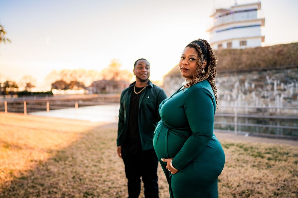 Pregnant woman in teal dress poses with partner outdoors during golden hour maternity photoshoot.