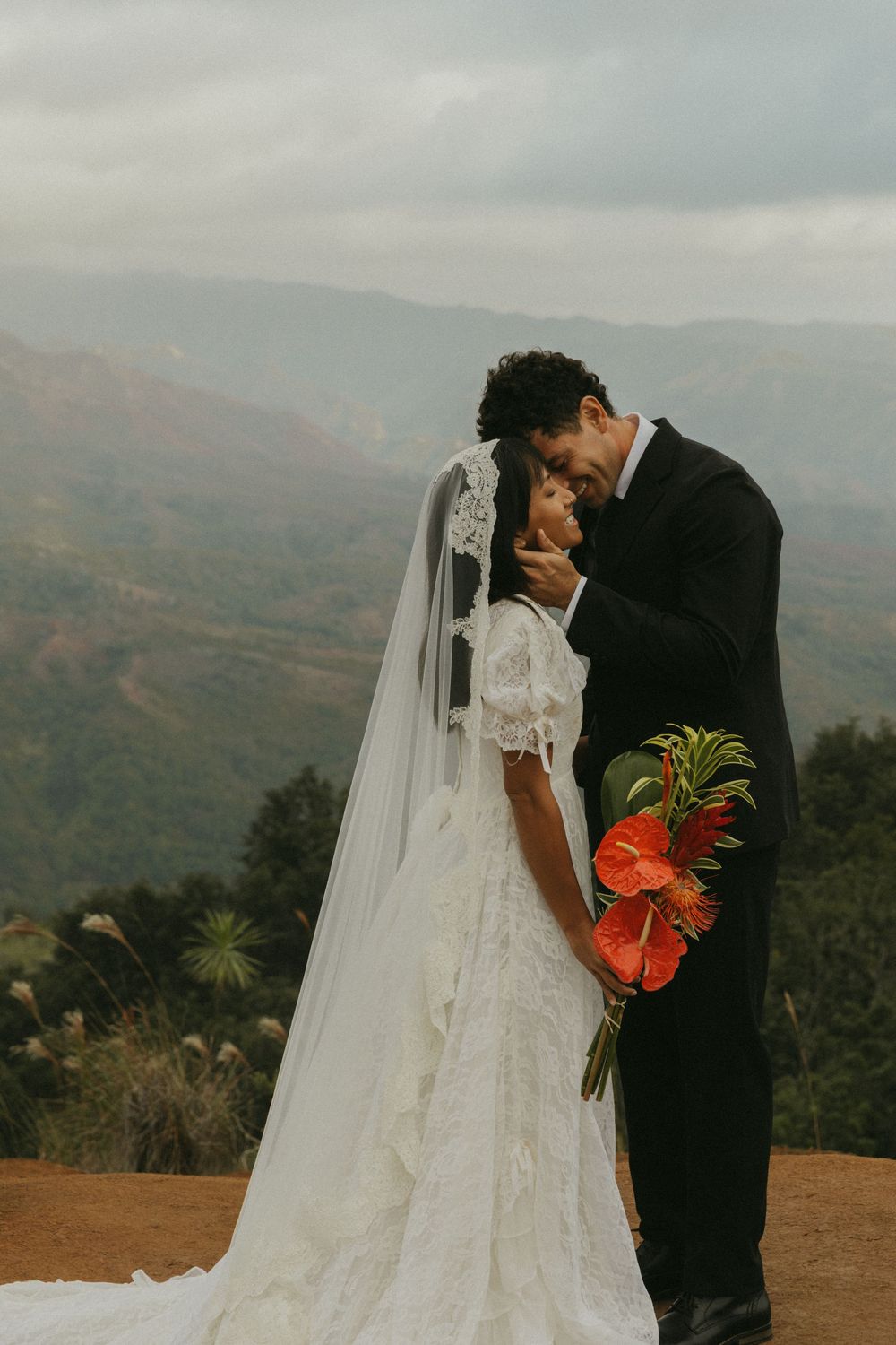 A romantic wedding moment captured against a misty mountain backdrop with a flowing white dress and vibrant orange bouquet.